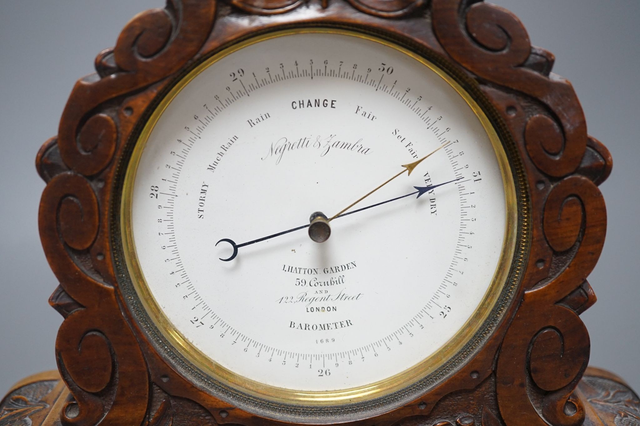 A late Victorian carved walnut aneroid mantel barometer by Negretti and Zambra, 34 cms wide